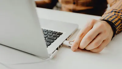 A person's hand inserting a white USB dongle into the side port of a silver laptop.