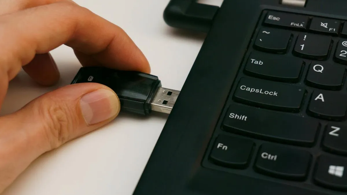 A hand inserts a black USB dongle into the side port of a dark laptop.
