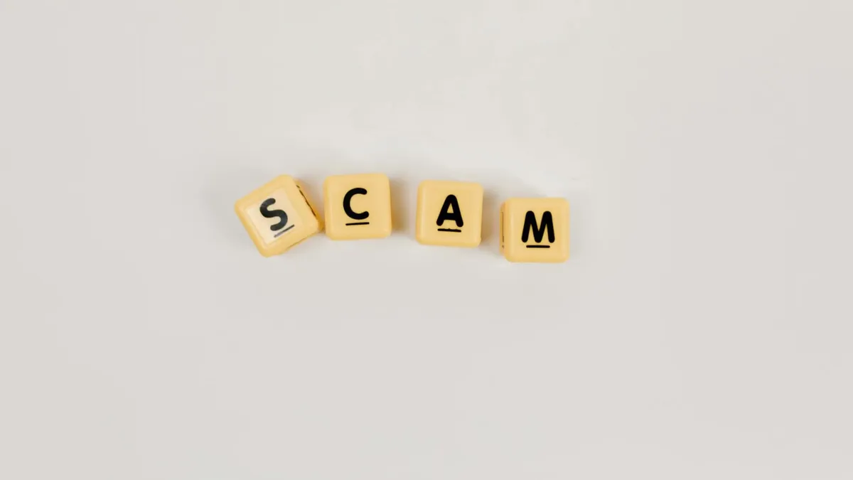 Four Scrabble tiles forming the word 'SCAM' on a neutral background, highlighting concepts like deceit.