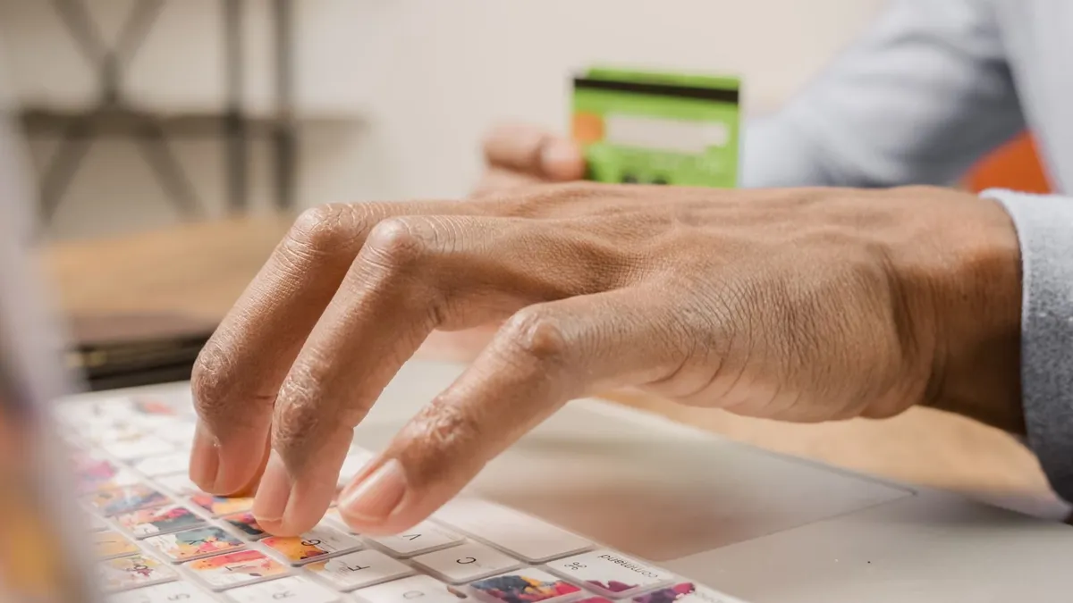 Person typing on a colorful laptop keyboard while holding a credit card, ideal for online shopping themes.