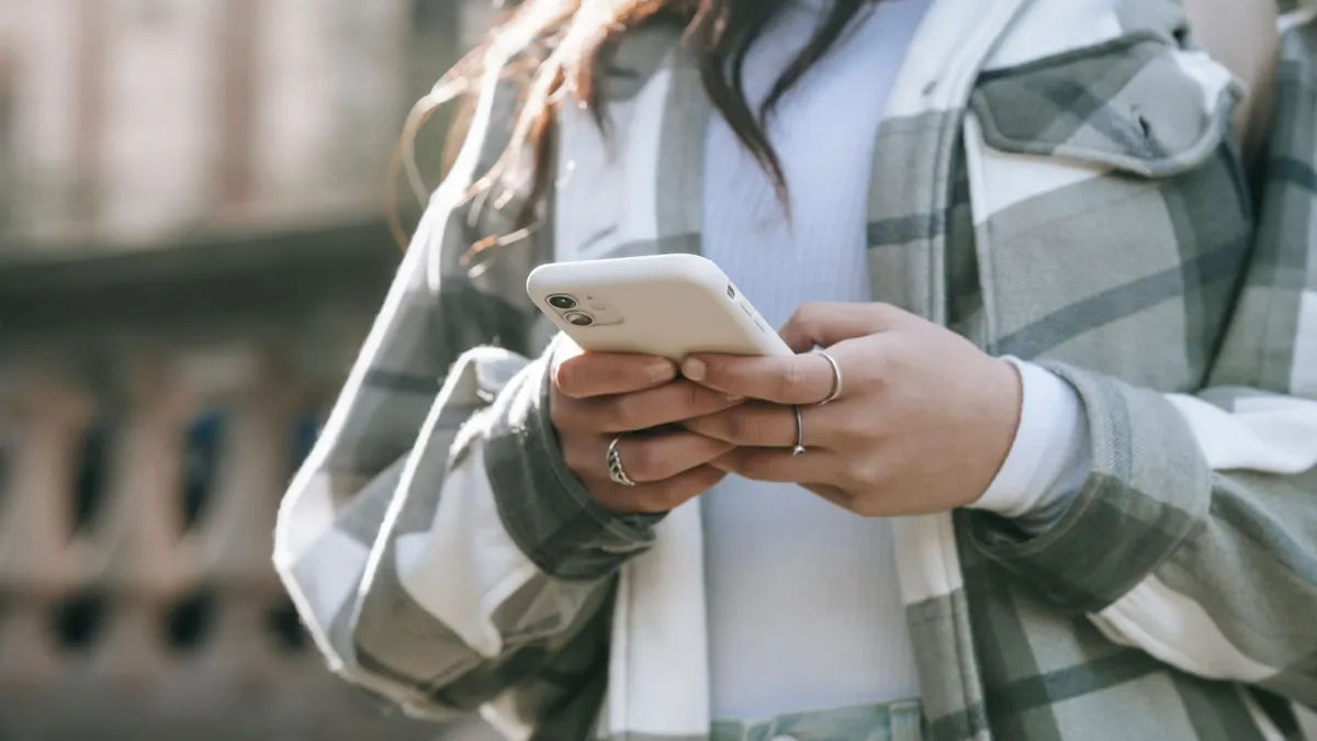 Crop faceless young woman in casual outfit text messaging on phone in city street in daytime