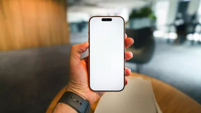 A hand holds a modern smartphone with a blank white screen, ready for content.