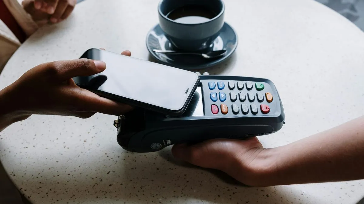 A person holding a smartphone over a payment terminal for a contactless transaction.