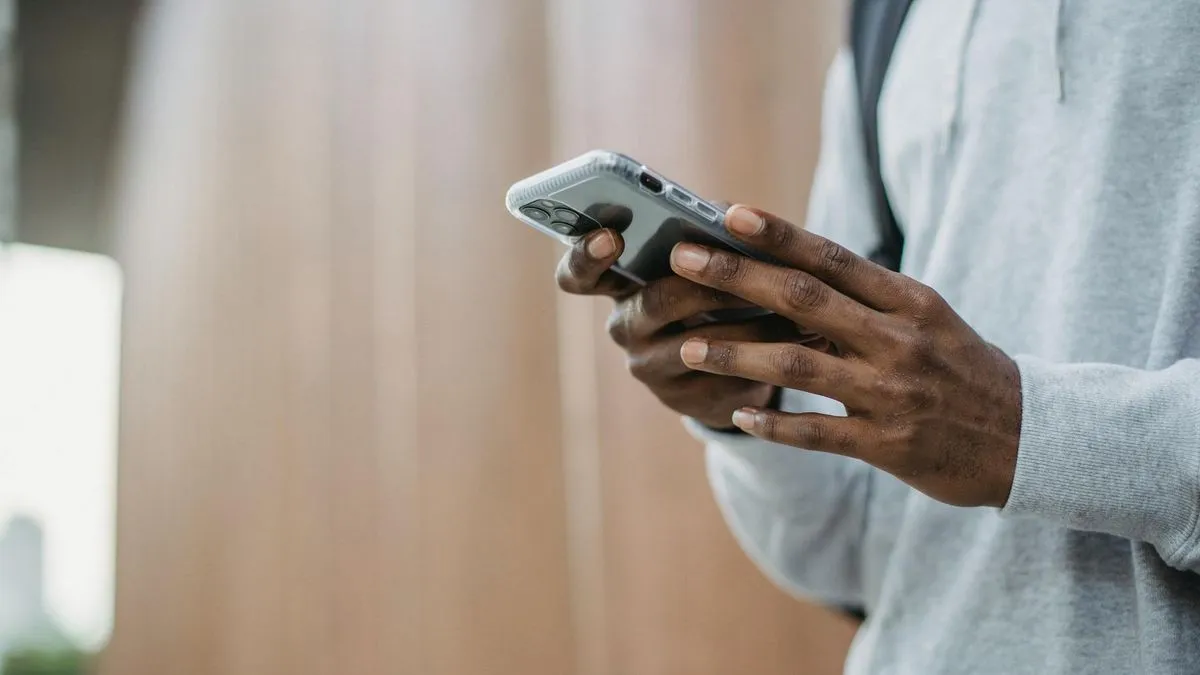 A person in a grey hoodie holds a smartphone with both hands, looking at the screen.