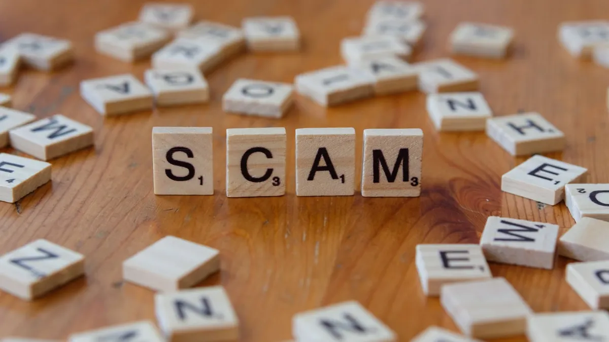 Image of Scrabble tiles spelling 'scam' surrounded by scattered letters on a wooden table.