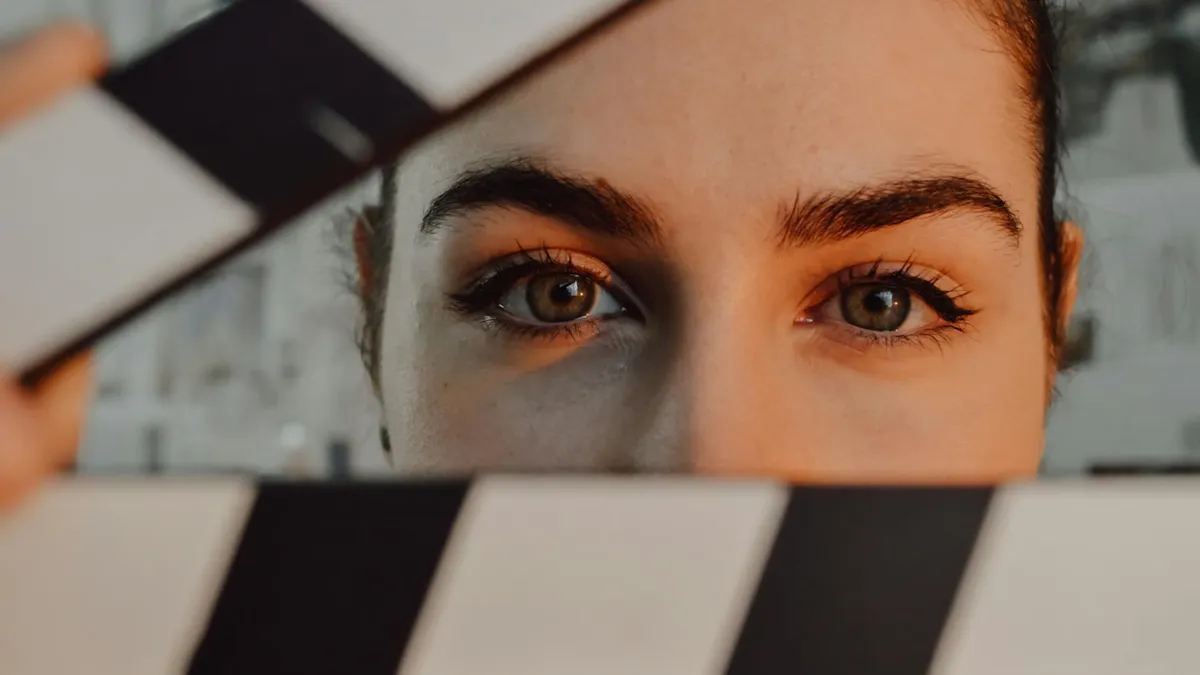 Intriguing close-up of a person's eyes behind a movie clapperboard, symbolizing filmmaking artistry.