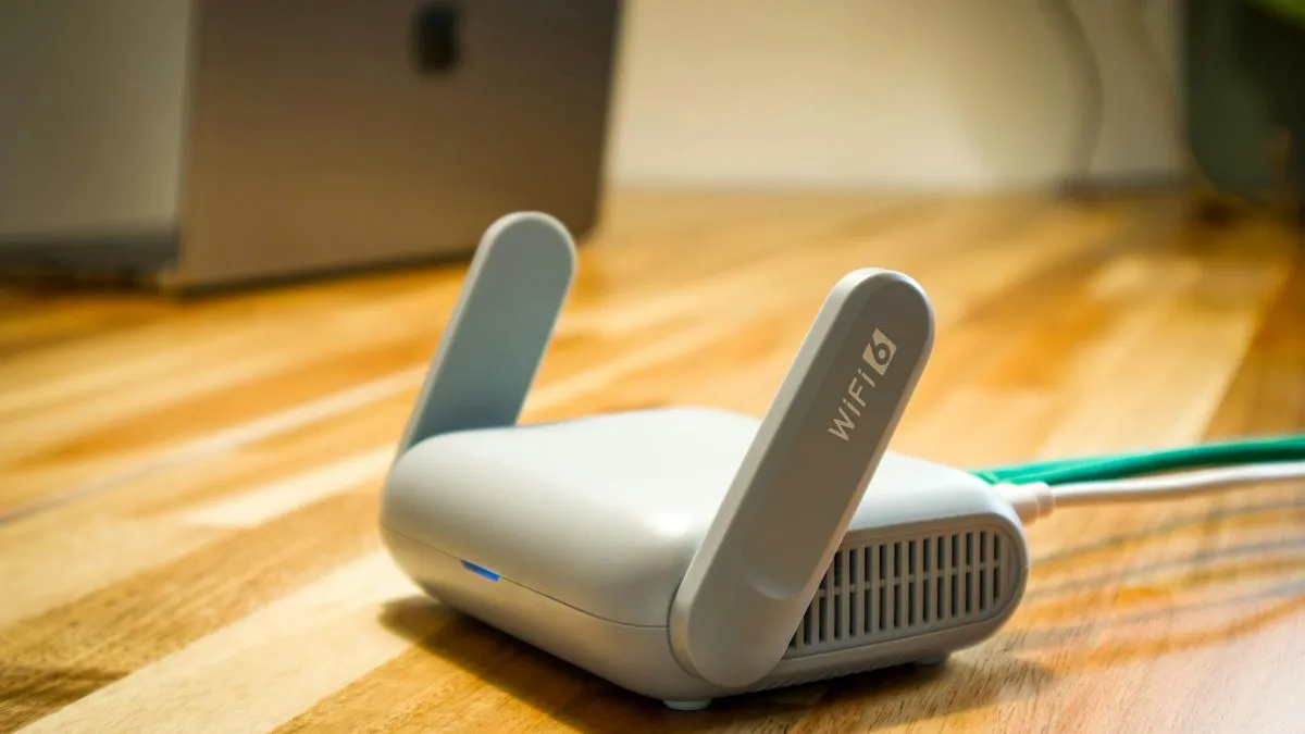 A small white WiFi router with two antennas and a green cable connected, on a wooden surface.