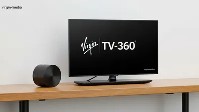 A black TV screen displaying 'Virgin TV-360' in white text, next to a black cylindrical device, on a wooden surface.