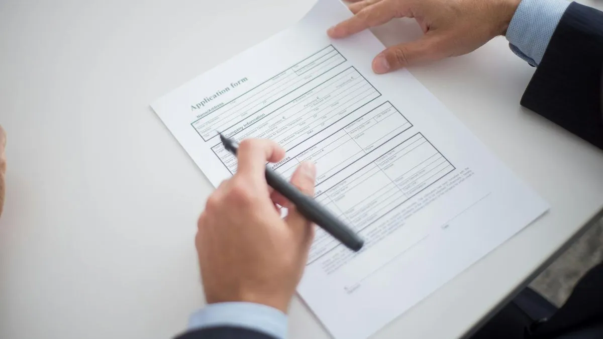 Close-up of a person's hands filling out an application form with a pen on a white desk.