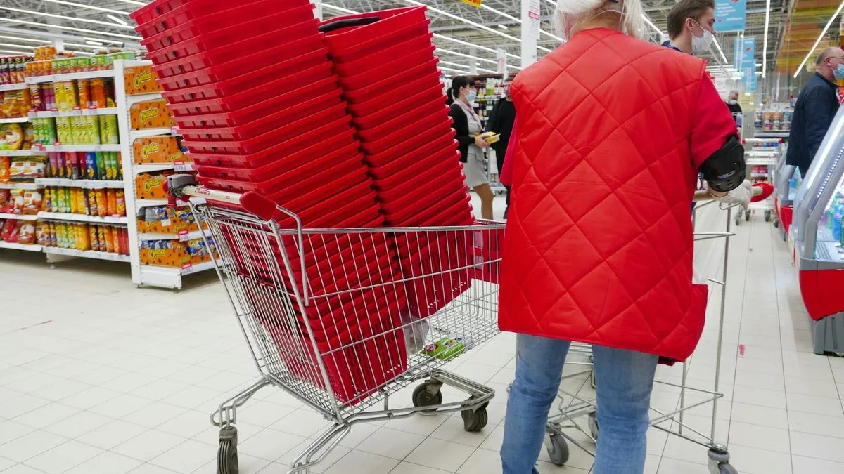 A person in a red jacket pushes a shopping cart filled with red baskets inside a supermarket.