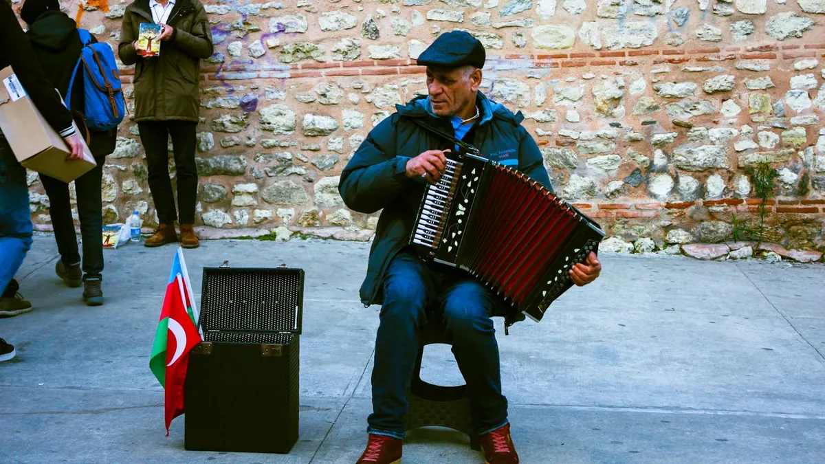 A street musician plays an accordion beside a stone wall in Istanbul, capturing the urban vibe.