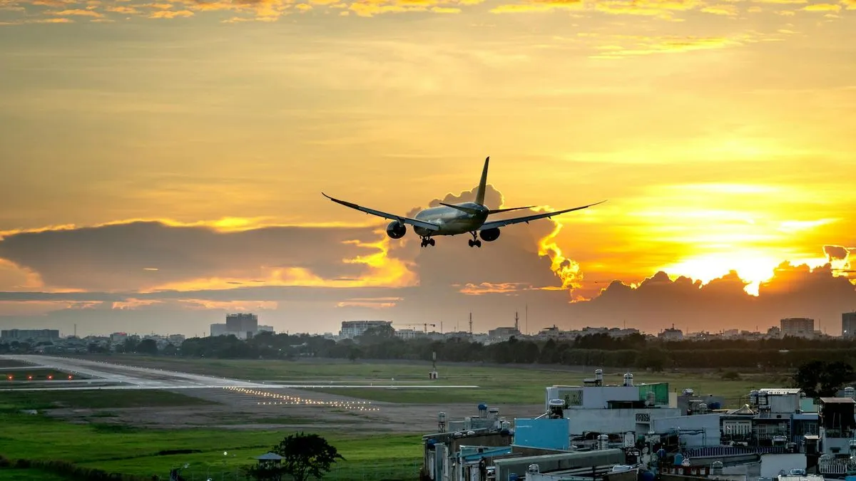 An airplane descends towards a runway at sunset, with a city skyline in the background.