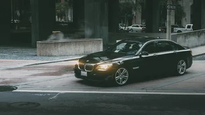 A black BMW car parked on a city street with buildings in the background.