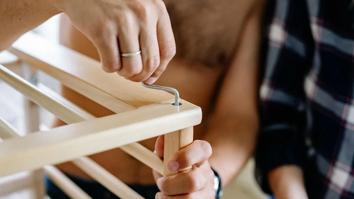 Close-up of hands assembling wooden furniture with an Allen key, suggesting DIY or flat-pack.
