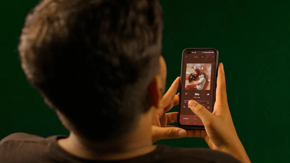 A person using a smartphone to stream music from a streaming service app indoors.