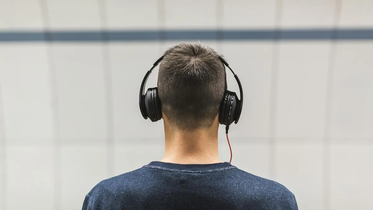 A person from behind wearing black over-ear headphones, listening to music against a plain background.