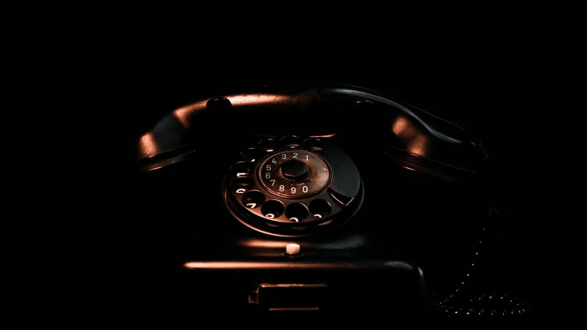 Vintage black rotary phone in a dark setting highlighting its classic design and retro appeal.
