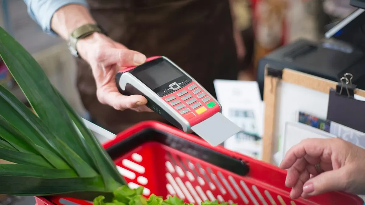 A customer inserts a card into a payment terminal held by a cashier at a grocery store.