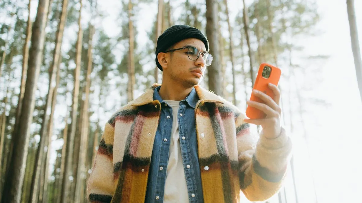 A man in a forest looking at his phone, possibly checking for signal or a map.