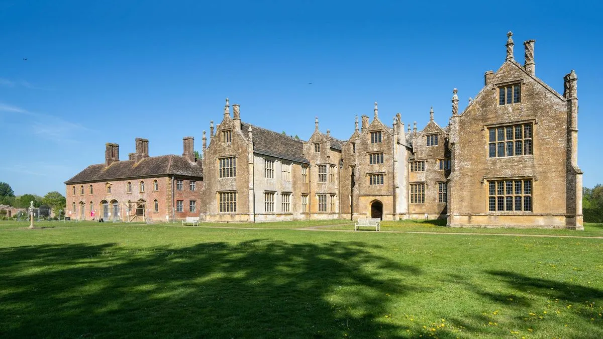 A wide shot of a large, historic manor house with extensive green lawns under a clear blue sky.