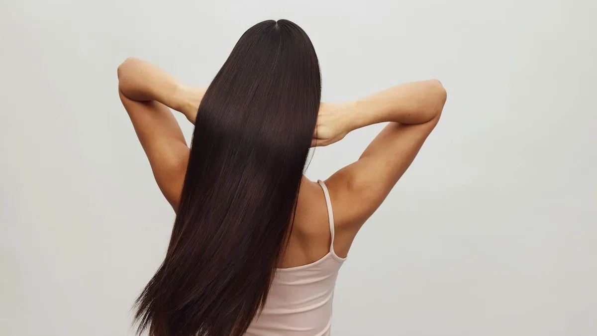 A woman with long, straight dark hair, seen from behind, posing with her arms raised.