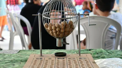 A bingo cage with wooden balls inside sits on a table with a bingo board.