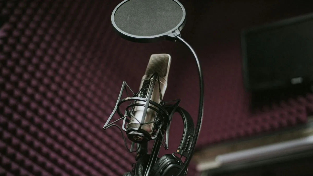 A close-up of a professional studio microphone with a pop filter and headphones in a soundproofed room.