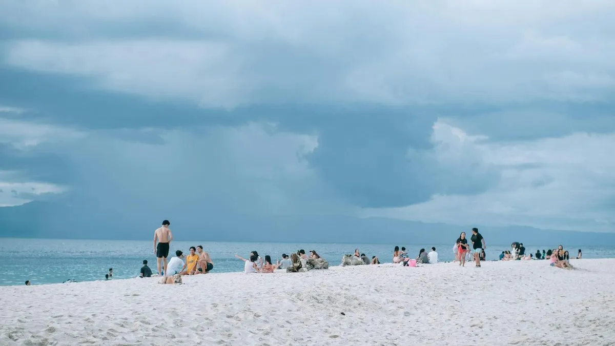 A wide shot of a sandy beach with many people relaxing and swimming in the ocean.