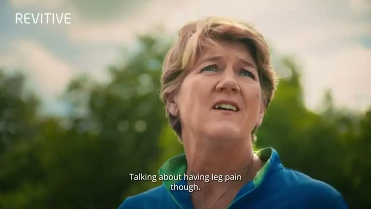 A close-up of Clare Balding looking up, outdoors with green trees in the background.