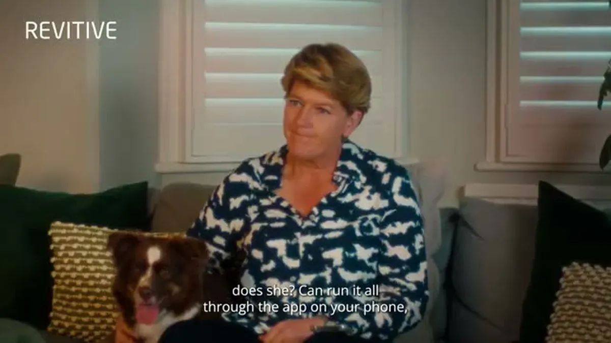 Clare Balding, a woman with short blonde hair, sits on a couch with a small brown and white dog.