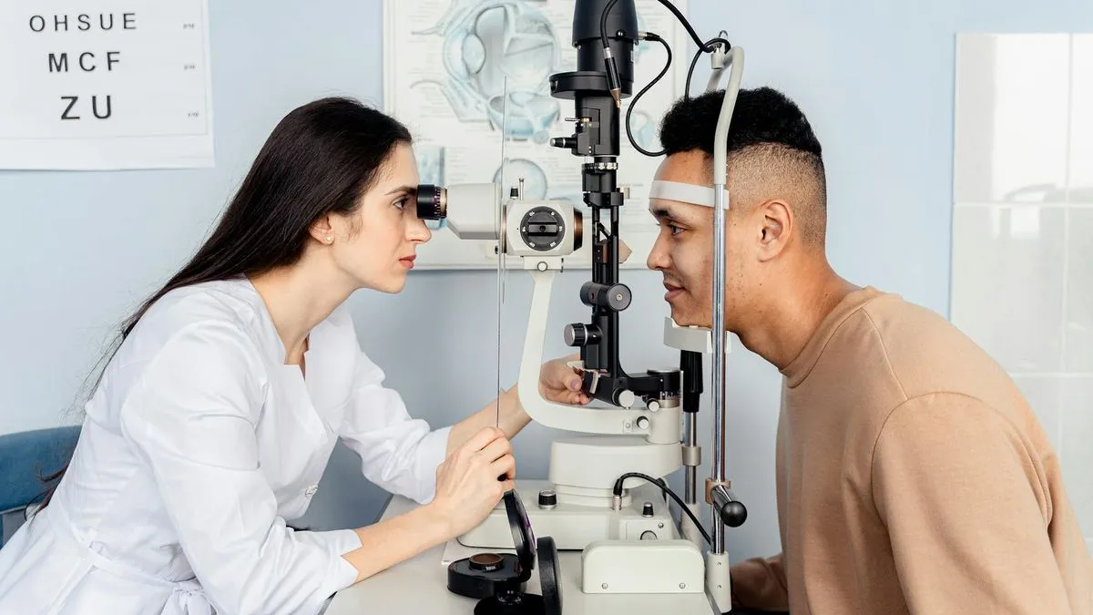 An optometrist in a white coat examines a male patient's eyes with a phoropter.