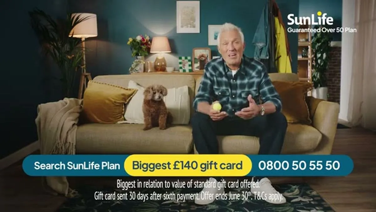 A wide shot of Martin Kemp sitting on a sofa with a small brown dog, holding a yellow ball.