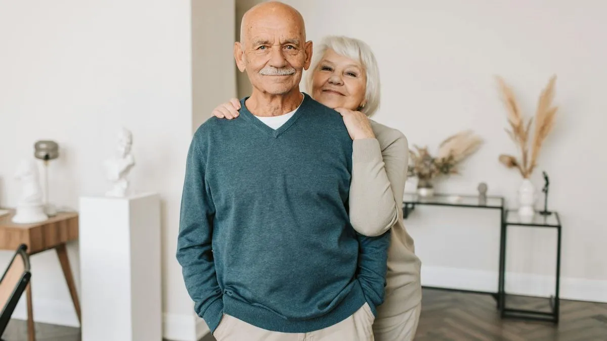 An older couple smiling at the camera, the woman's arm around the man's shoulder.