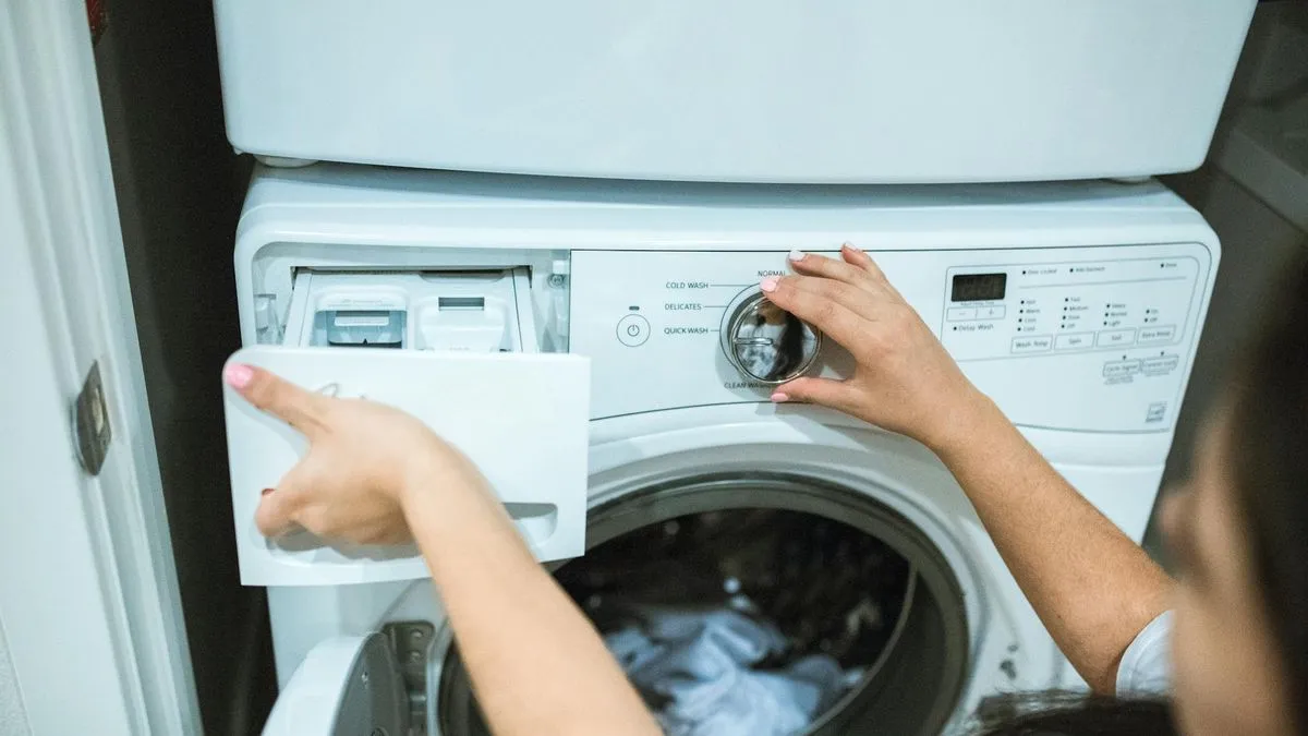A person's hands adjusting the settings and opening the detergent drawer of a washing machine.