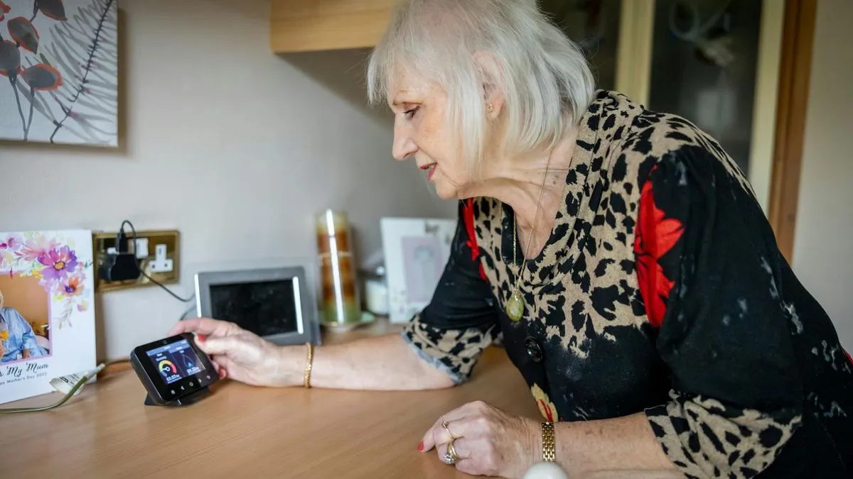 An older woman with white hair looks at a smart meter display on a wooden table.