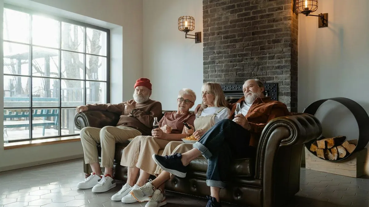 Four older adults sitting on a brown leather sofa, watching something and smiling.