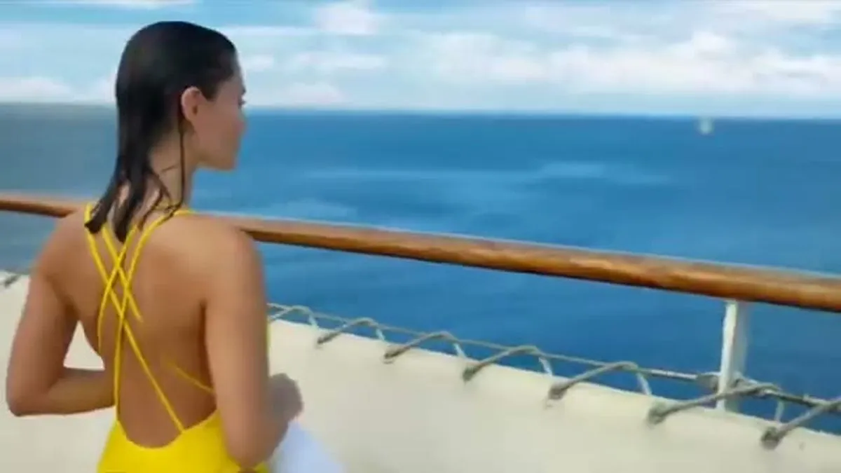 A woman in a yellow swimsuit looks out at the ocean from a ship's deck.