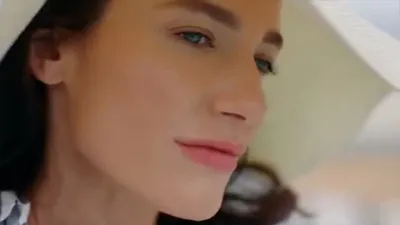 Close-up of a woman's face, looking down and to the right, wearing a white hat.