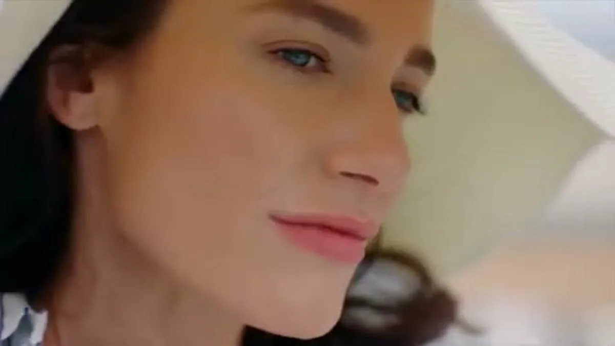 Close-up of a woman's face, looking down and to the right, wearing a white hat.