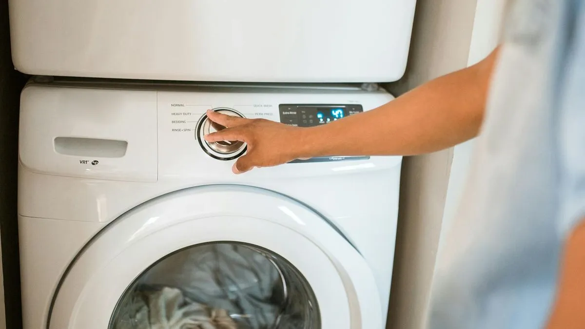 A person's hand adjusts the settings on a white washing machine with clothes inside.