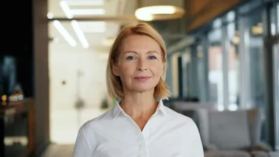 A confident blonde woman in a white shirt looks directly at the camera.