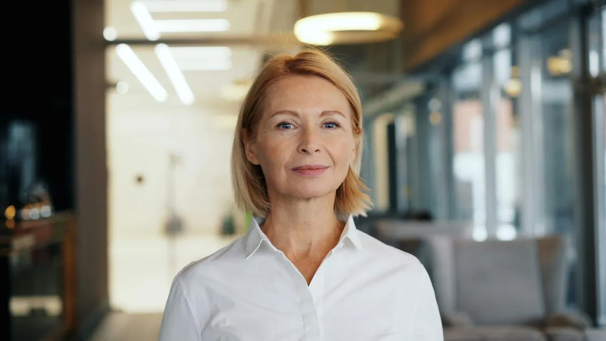 A confident blonde woman in a white shirt looks directly at the camera.