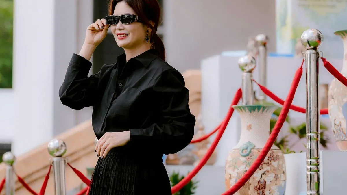 A smiling woman in a black shirt and sunglasses stands next to a red velvet rope.