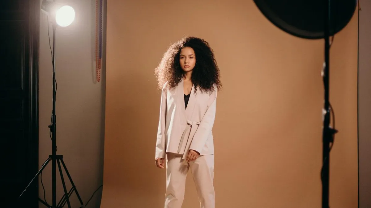 A woman with curly hair in a beige suit poses in a photo studio.