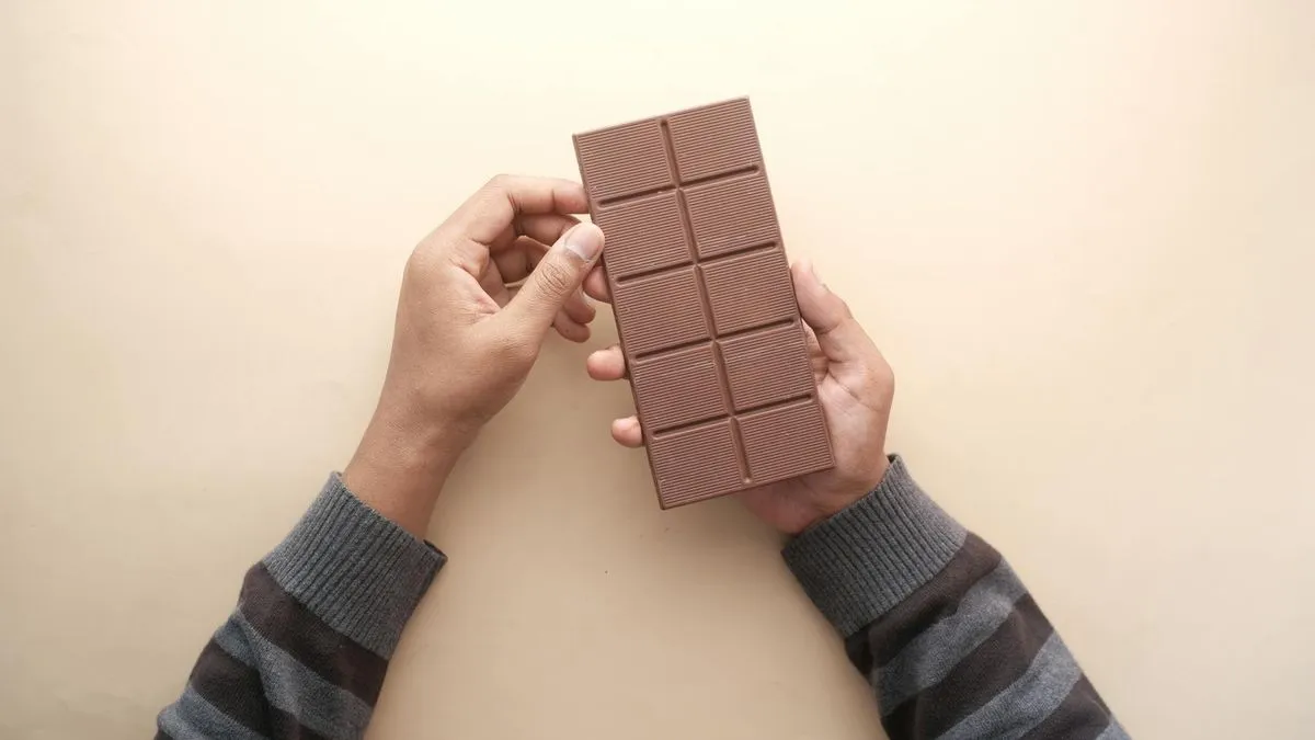 A person's hands holding a large, rectangular bar of milk chocolate against a light background.