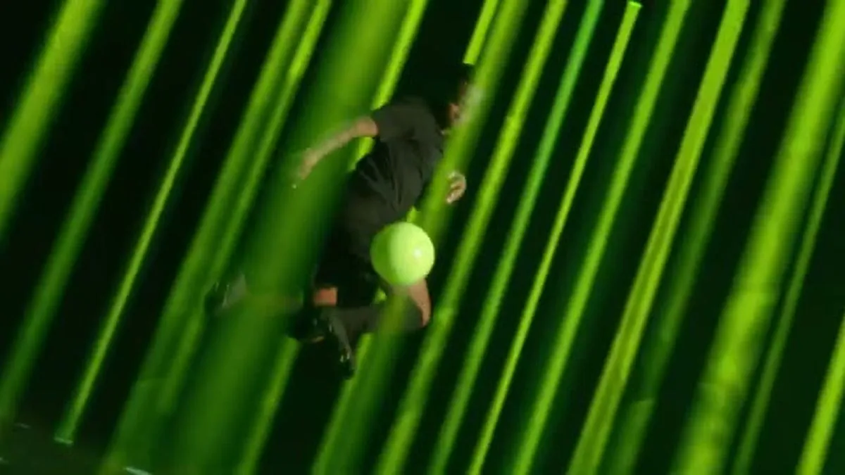 Raheem Sterling, in black athletic wear, is mid-air, kicking a bright green football against a backdrop of vertical green lights.