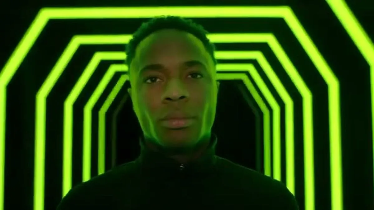 Raheem Sterling looks directly at the camera, framed by a neon green hexagonal tunnel.