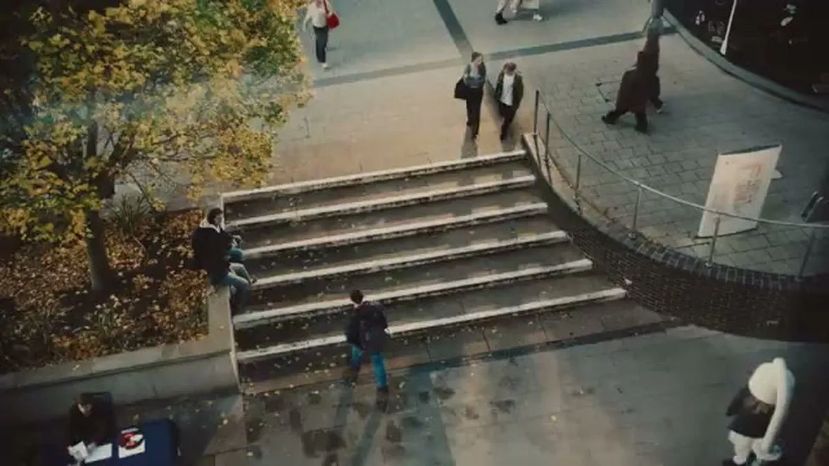 An overhead wide shot of a city square with people walking and sitting on steps.