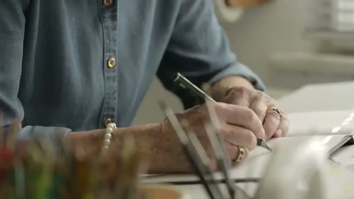 Close-up of Judith Kerr's hands drawing with a pencil on a white paper.
