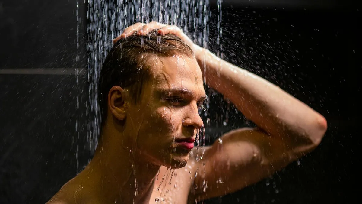 A man with wet hair and face is showering, with water cascading over his head.
